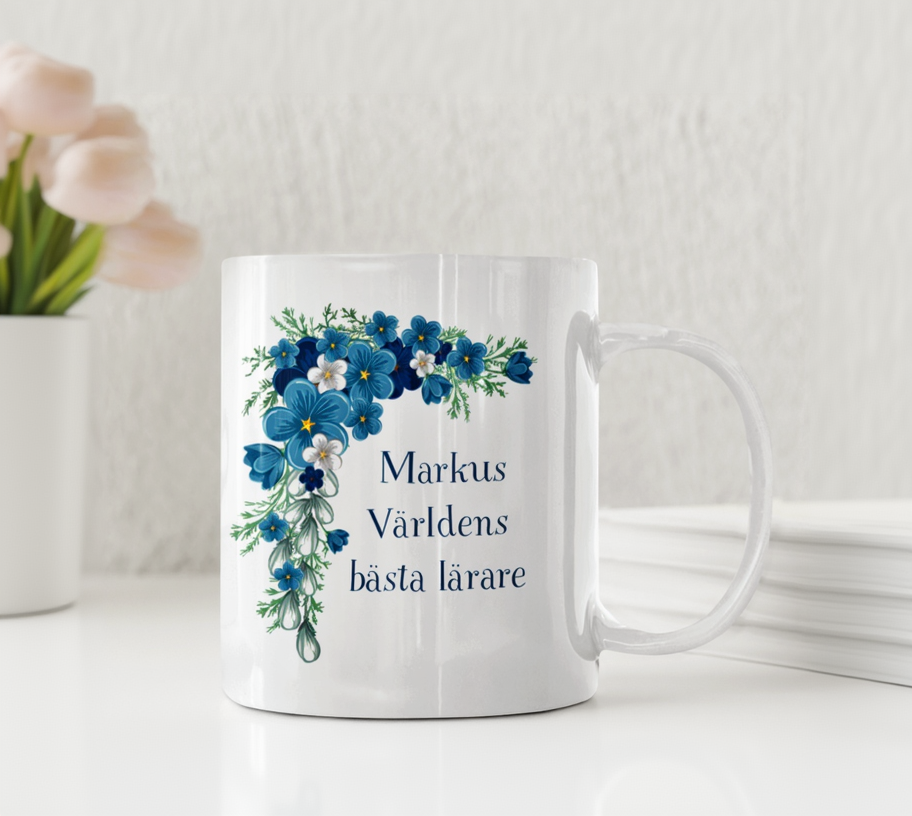Vit keramikmugg med blå blommor och texten Världens bästa lärare med ett personligt namn.