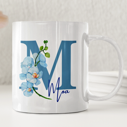 Vit keramikmugg dekorerad med en elegant blå orkidé och valfri personlig text. Dalastil mugg